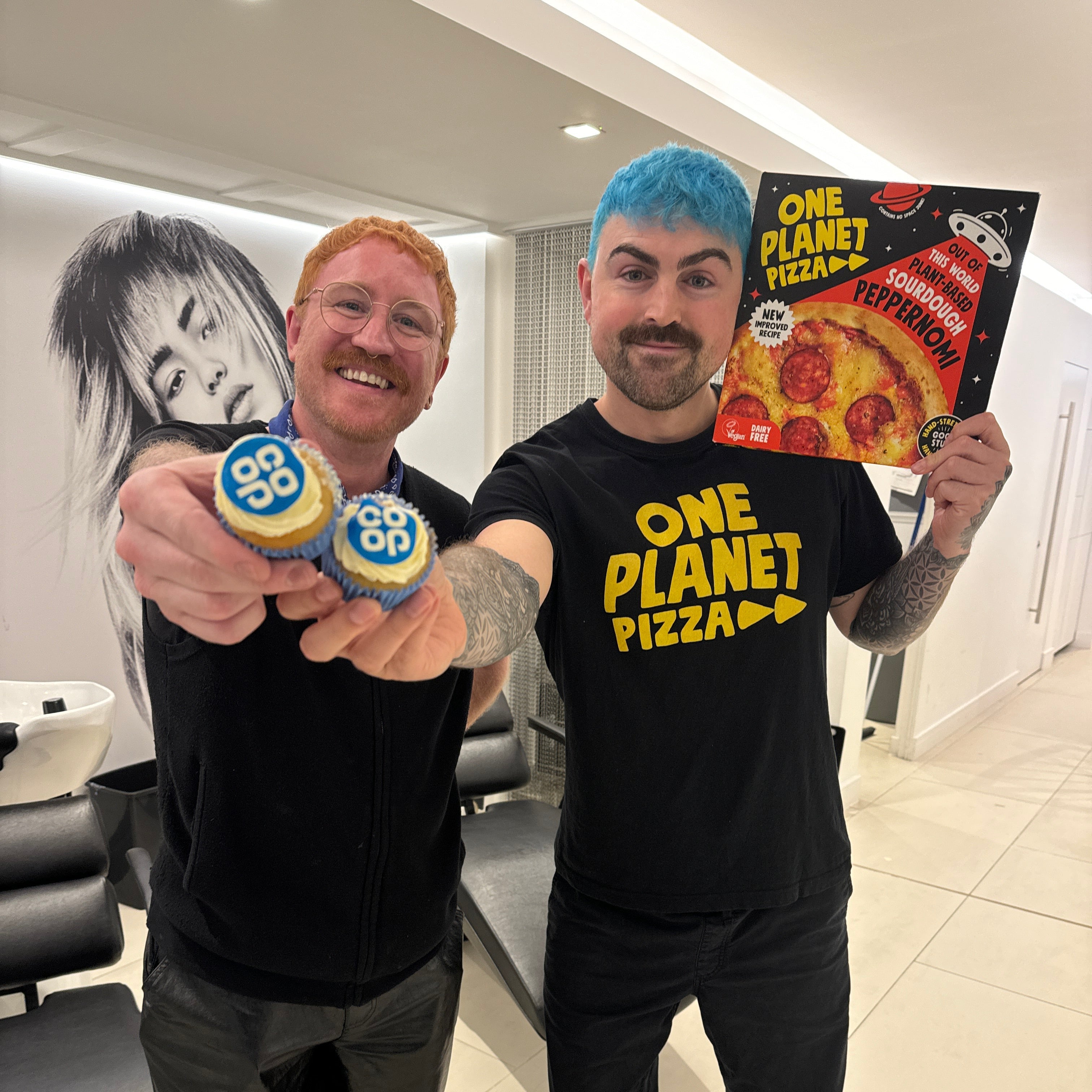 Two people in a room with one holding a One Planet Pizza box.