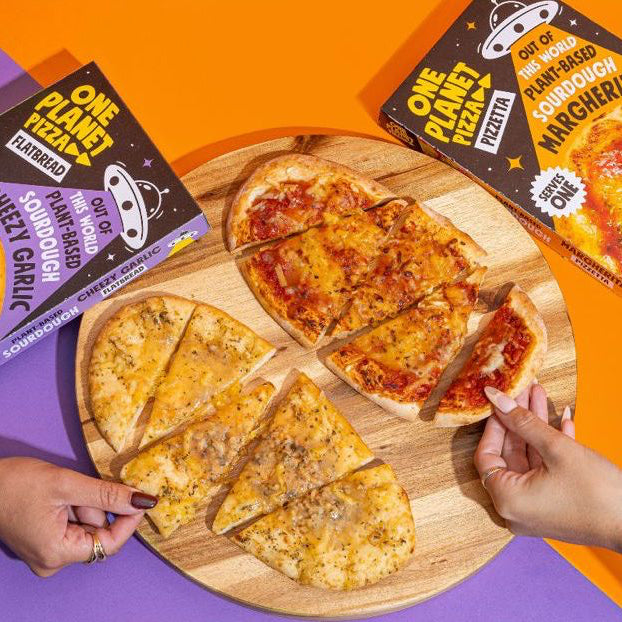 Wooden cutting board with sliced pizzas and 'One Planet' pizza boxes on a colorful background