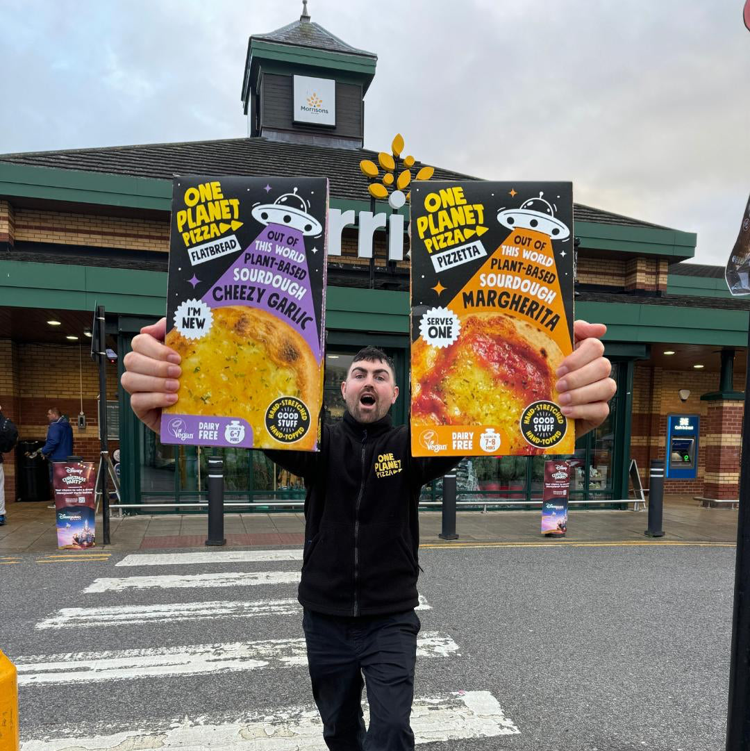 Joe  holding two boxes of One Planet Pizza in front of a store.